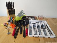 Full view of assorted kitchen tools including knives in block, kitchen utensils, measuring tools, silverware tray, chopsticks, and cutting boards.