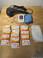 Full lot overview showing electric back massager, digital blood pressure monitor with cuff, and 12 instant hot packs with fabric covers arranged on a wooden surface.