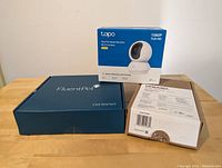 FluentPet Basic Kit box, Dremel PawControl box, TP-Link Tapo pet camera box on wooden surface.