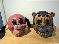 Two Umbrella Academy replica masks displayed together on a table, seen from front and slightly angled showing details.