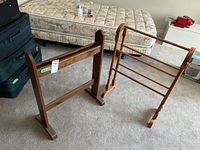 Two wooden blanket racks placed side by side on carpeted floor in front of a mattress and suitcases.