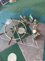 Full view of the brass ship steering wheel, brass bell, three brass horse figurines, and brass trinket box on a carpet.