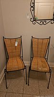 Two wicker and metal chairs side by side against a wall with mirror above.