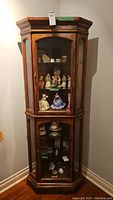 Front view of the wood corner display cabinet filled with figurines, showing glass doors and interior shelves.