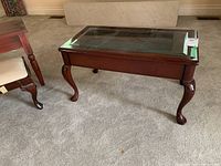 Wooden coffee table with glass top showing leg details and overall form in carpeted living room.