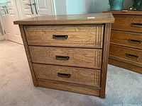 Front view of three-drawer dresser showing wood grain finish and metal bail handles