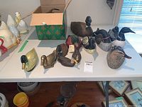 Overview of twelve decoys and bird figurines on a folding table