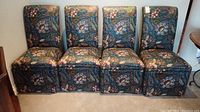 Four upholstered chairs with floral paisley fabric, aligned side by side against wall.