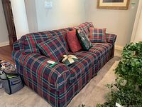 Side angle view of the plaid upholstered sofa with cushions and arm covers, showing pattern and arm details.