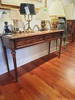Angle view of wood hall table with 2 drawers showing front and one side with lamps on top.