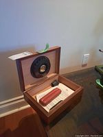 Humidor box open on table showing hygrometer mounted in lid, leather case, funnel, cutter, instruction sheet inside