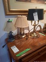 Photo of three table lamps arranged on wood furniture, showing different bases and fabric/glass shades.