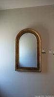 Full front view of arched gold framed mirror on a beige wall