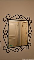 Front view of rectangular mirror with decorative black metal frame and scrollwork mounted on wall