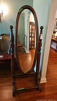 Front view of wood framed oval mirror showing full length and wood stand.