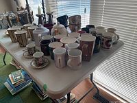 Full view of table with assorted mugs, teapots, and saucers arranged, showing variety and quantity