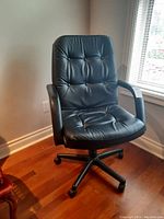Front angled view showing padded seat, backrest with button tufting, and armrests on the black faux leather office chair.