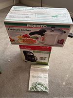 Presto pressure cooker box on top, Sunbeam TeaDrop tea maker box below, Salad greens dryer bag in front, all arranged clearly.