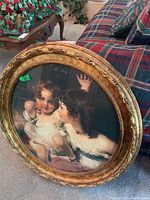 Close-up photo of the round framed print showing detailed carved gold frame and part of the children portrait.