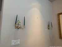 Two brass wall sconces mounted on a wall, each holding two black taper candles.