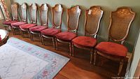 Ten Sklar Peppler wood framed chairs with red upholstered seats and cane backs, lined up side by side against a wall showing overall condition