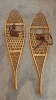 Full view of both vintage Rebaf snowshoes showing wooden frame, webbing, and leather bindings.