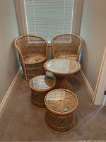 Two wicker chairs and three wicker tables with glass tops arranged against a window