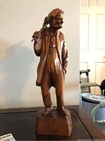 Front view of the wood sculpture showing an old man with a sack over shoulder