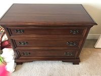 Front view of cherry wood chest with three closed drawers and metal handles.