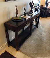 Side angle view showing two-section console table, dark wood, brass handles on drawers, sculptures on top, and rattan lower shelf.