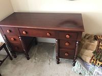 Photo showing the full wood dresser with seven drawers and turned legs, highlighting overall design and condition.