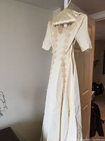 Full front view of cream-colored formal wedding dress with beige floral applique trim on bodice and skirt, mid-length sleeves, hanging on padded hanger