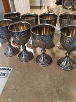 Photo showing the set of six silver-toned goblet chalices on a countertop with detailed floral designs on each cup and base.