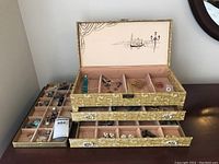 Wide angle photo of fabric-covered jewelry box with pink velvet interior and assorted costume jewelry inside compartments and drawers.