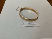 Front view of rolled gold filled hinged bangle bracelet with engraving and safety chain visible