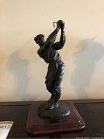 Front angle of the bronze golfer sculpture on wooden base showing the golfer mid-swing and plaque details.