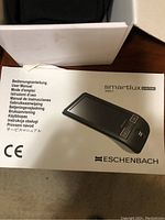 User manual for Eschenbach Smartlux Digital 165011 in multiple languages alongside white box.