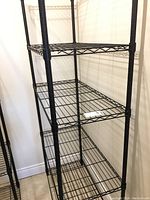 Front view of the four-shelf black metal wire shelving unit showing wire mesh shelves and vertical legs.