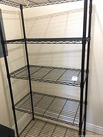Full view of four-shelf black metal wire shelving unit in corner of room.