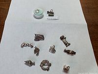Photo showing all 9 sterling charms arranged on white paper, highlighting shapes and details for identification.