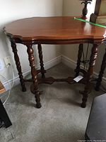 Full side view of wooden table showing scalloped top edge, turned legs and stretchers, with carpeted floor in background.