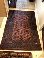 Full view of large reddish rug with multiple oval motifs and intricate dark border on floor.