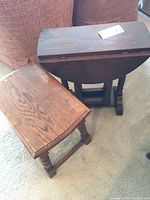 Photo of wooden table and stool showing table top with foldable leaves and stool beside it on carpeted floor