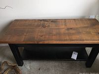 Full view of the rectangular wooden table showing natural wood top and black painted base with lower shelf.