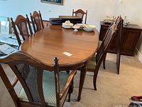 Full view of wooden oval dining table with six matching chairs around it in a carpeted room.