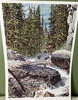 Photo of a signed print titled Montana Spring featuring a forest, boulders, stream, and deer.