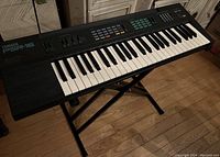 Yamaha PSR-16 keyboard on black X-style stand, showing full keyboard length and keys with wood floor background.