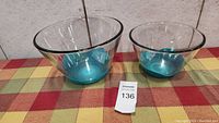 Two turquoise glass nesting bowls, larger and smaller, on a checkered cloth