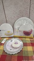 3 Wilton cake decorating items: 10 inch cake pan, 3-pack 12 inch platters, and 12 inch scalloped edge cake board all new and sealed in packaging