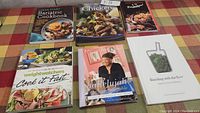 Six cookbooks arranged on a tablecloth with colorful covers showing distinct titles and food images, providing full view of the lot.